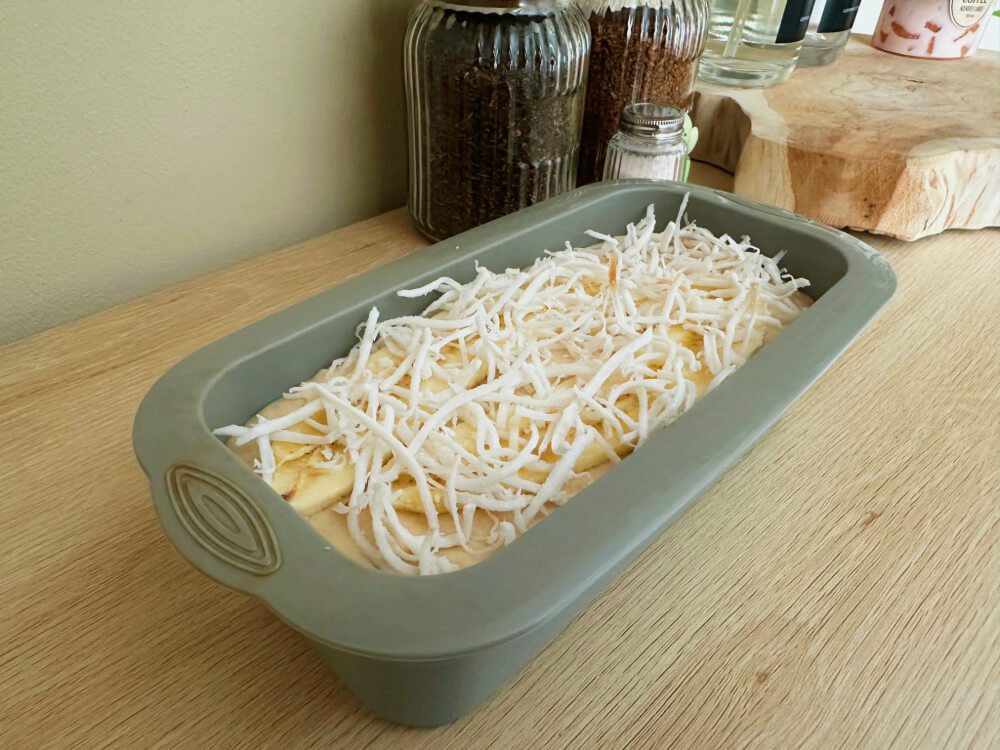 Fertigen Teig in längliche Kuchenform geben und mit Banane und Kokosraspeln toppen, fünfter Schritt für den Bananenkuchen-Teig.